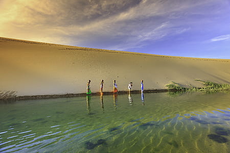 woman wearing assorted dresses near body of water on desert under white clouds thumbnail