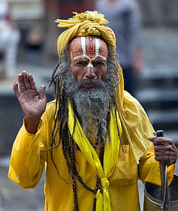man wearing yellow holding wooden rod and raising right palm thumbnail
