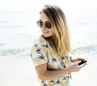 smiling woman holding smartphone while standing on shore during daytime thumbnail