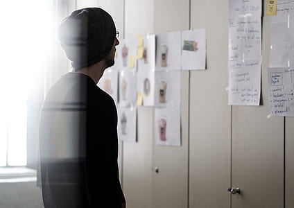 man in black sweater looking at wall with assorted papers thumbnail