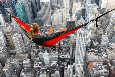 woman sitting on and red hammock overlooking high-rise buildings thumbnail