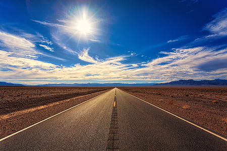 gray asphalt road between desert field during daytime thumbnail