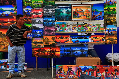 man standing beside paintings thumbnail