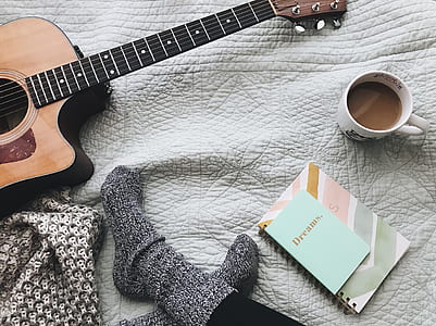 person in pair of gray socks sitting in front of acoustic guitar, coffee mug, and spiral notebook thumbnail