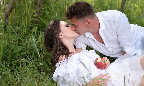 man and woman kissing while lying near green plants at daytime thumbnail