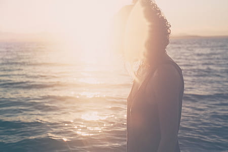 woman wearing black tank top standing beside body of water during sunset thumbnail