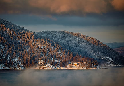 house near body of water surrounded by trees near mountain thumbnail