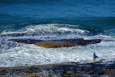 person standing on rock surrounded of ocean during daytime thumbnail
