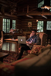 man sitting on padded chair while using laptop inside room thumbnail