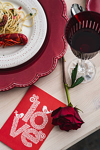 Fancy dinner with seafood pasta, crayfish and red wine by the table decorated with roses thumbnail