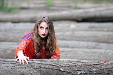 woman in orange floral long-sleeve shirt standing on logs during daytime thumbnail