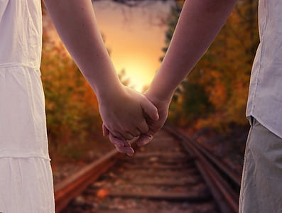 two people holding hands standing on train rail during daytime thumbnail
