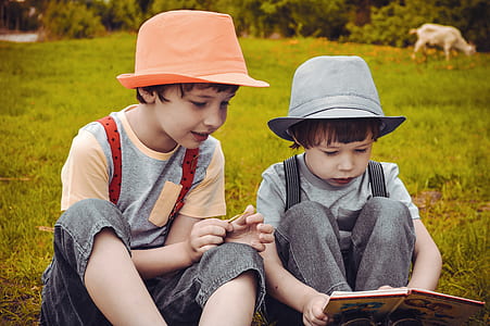 two boy sitting on green grass reading book during day thumbnail