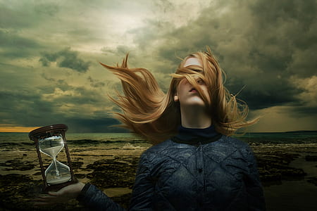 photo of woman holding sand hour glass near seashore under nimbus clouds thumbnail
