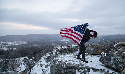 man holding USA flag on rock during daytime thumbnail