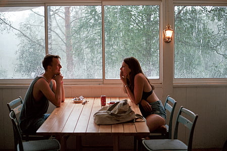 woman sitting on chair looking man sitting on chair on the opposite of table's eye beside window during daytime thumbnail