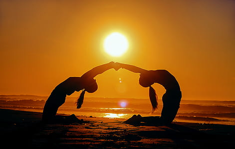 two women creating heart form pose in the sand under golden hour photography thumbnail