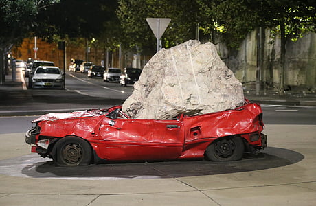 red car squashed by gray stone thumbnail