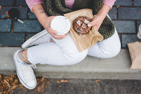 woman sitting on pavement holding disposable cup and donut thumbnail