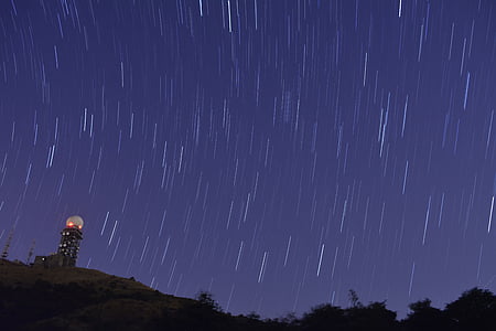 timelapse photography of silhouette of tower near trees under starry sky thumbnail
