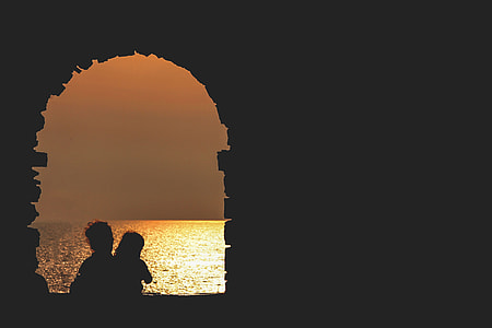 silhouette photo of two person on window facing body of water during sunset thumbnail