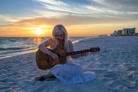 woman in white dress sitting on white sand while playing a guitar thumbnail