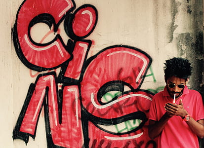man smoking beside white and red graffiti wall thumbnail