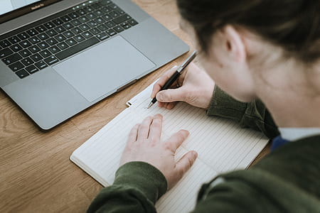 woman writing on lined paper near MacBook Pro thumbnail
