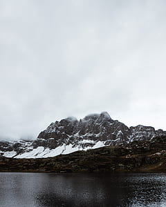brown mountain covered by snow near body of water during daytime thumbnail