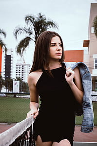 woman in black spaghetti strap dress holding blue denim jacket during daytime thumbnail