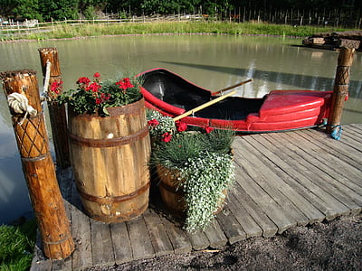 red boat docked near barrel and red petaled flowers thumbnail