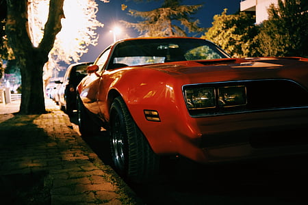 orange sports coupe on road beside tree at nighttime thumbnail