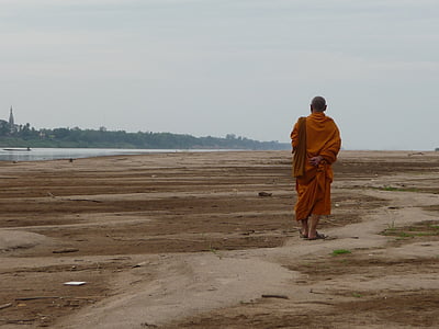monk walking on soil beside water and forest thumbnail