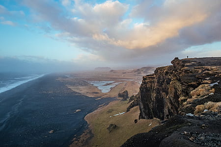 silhouette of a person on cliff near body of water during daytime thumbnail