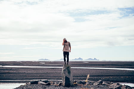 A young Caucasian wearing hooded sweatshirt man standing on a tall rock thumbnail