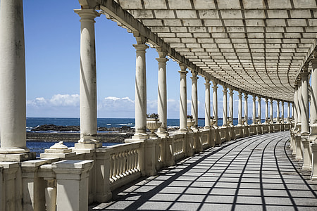 pathway with white columns and roof near blue sea at daytime architectural photography thumbnail