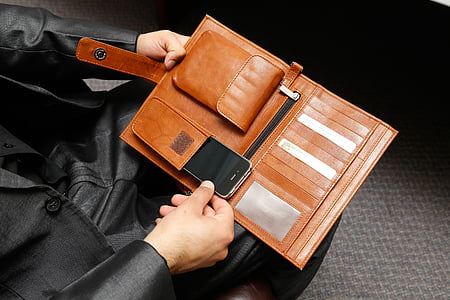 person holding brown leather wallet with smartphone thumbnail