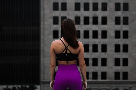 woman in black sports bra and pink yoga pants facing gray building thumbnail