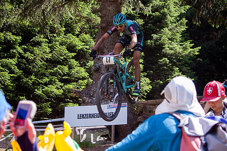 man riding mountain bike dropping near tree and people thumbnail
