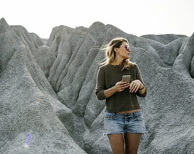 selective color photography of woman standing near mountain ride while holding smartphone thumbnail