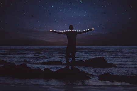 silhouette of a man standing on rock next to beach thumbnail