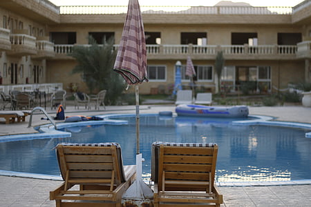 two brown wooden loungers facing pool thumbnail