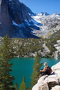 woman sitting on cliff in front of body of water thumbnail