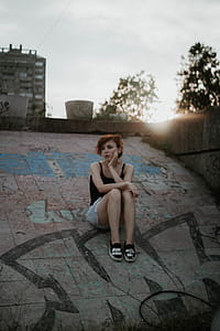 Woman Wearing Black Tank Top Sitting on Concrete Surface thumbnail