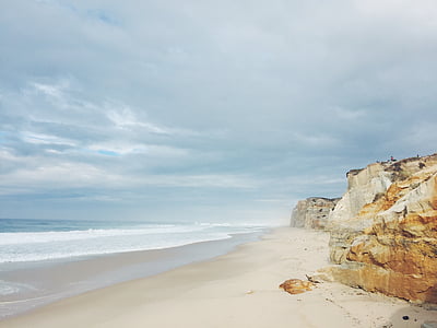 brown cliffs near seashore under cloudy sky thumbnail