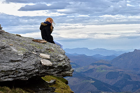 woman wearing parka coat sitting on cliff under blue sky thumbnail
