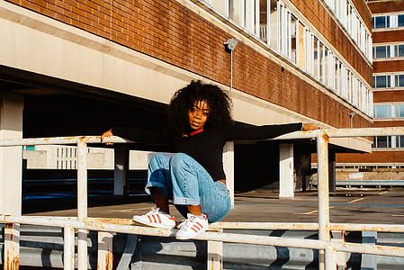 woman in black long-sleeved top sitting on white steel fence during daytime thumbnail