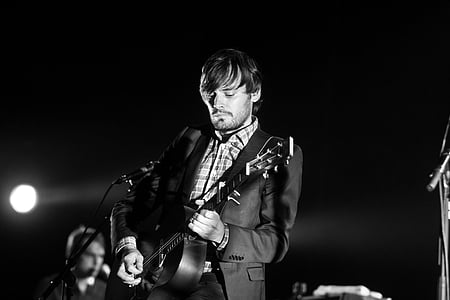 greyscale photo of man grey suit playing acoustic guitar on stage thumbnail