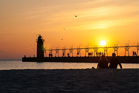 silhouette photo of man and woman sitting on shoreline during golden hour thumbnail