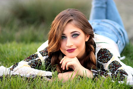 woman in white and black top and blue jeans lying on green grass thumbnail